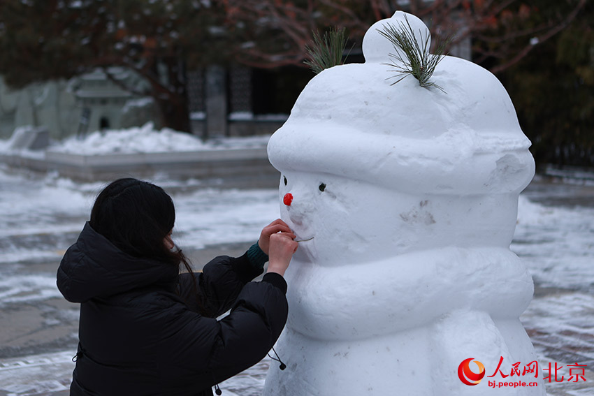 在西城区广宁公园，一个女孩用小树枝给雪人摆出嘴巴形状。郭斌摄